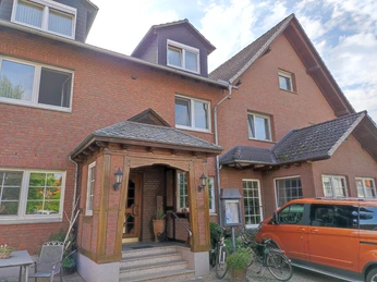 Außenanischt Schierbrucher Krug.jpg Rot verklinkertes Gasthaus mit Dreiecksgauben, Eingangsstufen und parkendem orangenen Auto davor.