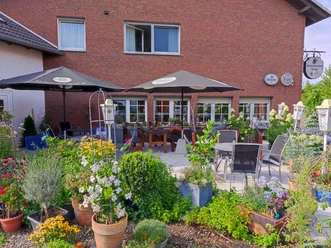 Der Biergarten des Schierbrucher Kruges bietet Sitzplätze im Freien, umgeben von blühenden Pflanzen.