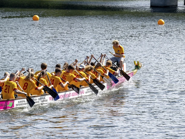 Drachenboot-Festival auf der Ruhr Eine Drachenbootmannschaft in gelben Trikots rudert synchron auf einem Fluss bei sonnigem Wetter.