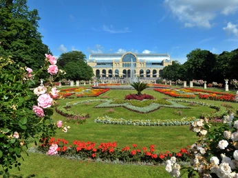 Flora Köln, Außenansicht Ein prachtvoller Rosengarten mit bunten Blumenrabatten vor einem historischen Gewächshaus.</p>A magnificent rose garden with colorful flower beds in front of a historic greenhouse.</p> <p
