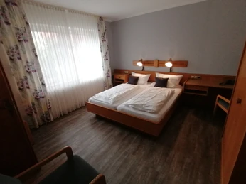 Helles, modern eingerichtetes Doppelzimmer mit zwei Betten, floral gemusterten Vorhängen und Schreibtisch.