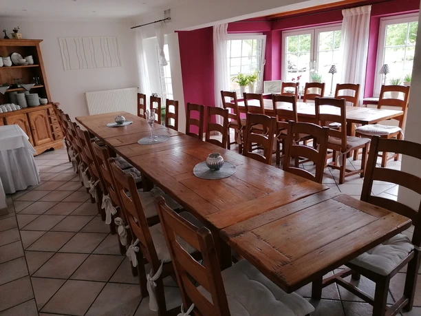 Ein großer Raum mit langen, hölzernen Tischen, dekoriert mit Kerzen, umgeben von Holzstühlen.