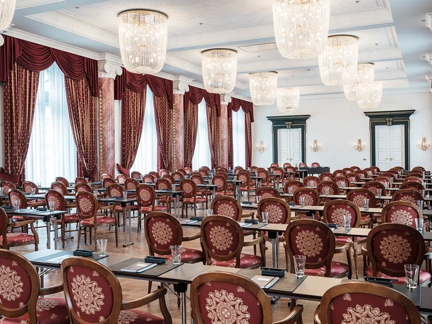 Ballsaal Althoff Grandhotel Schloss Bensberg An elegant conference room with red chairs, chandeliers and high windows.
