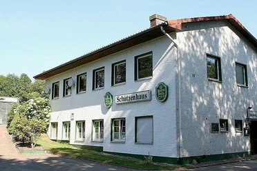 tengern-schuetzenhaus.jpg Zweigeschossiges Gebäude mit weißen Wänden und grünem Schild mit "Schützenhaus" im ruhigen Umfeld.