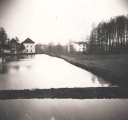 tengern-finkmanns-muehle-05.jpg Historische Windmühle am Seeufer mit spiegelndem Wasser, Bäumen im Hintergrund und vereinzelt Gebäuden.