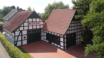 tengern-kutscherhaus-backhaus.jpg Fachwerkgebäude mit roten Ziegeldächern in bewaldeter Umgebung, umgeben von einer zum Teil gepflasterten Fläche.