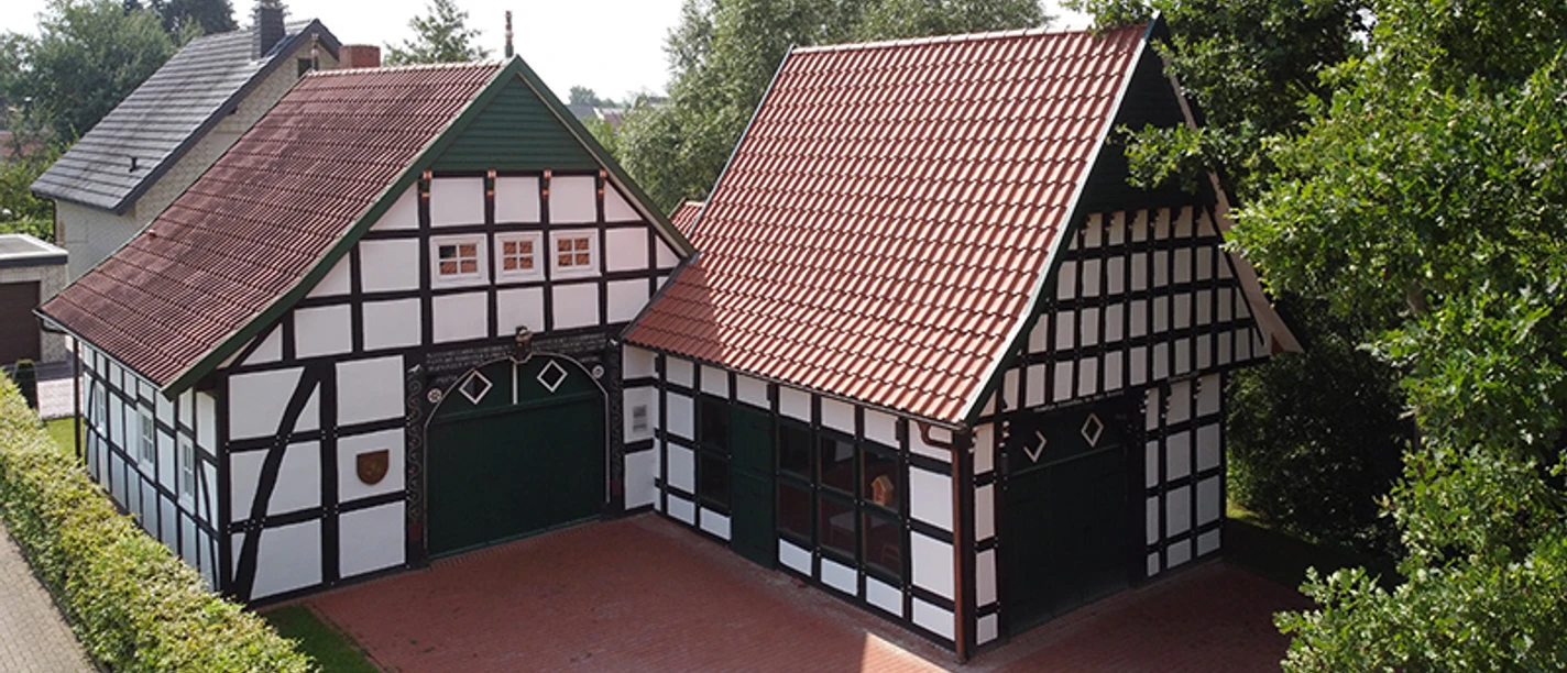tengern-kutscherhaus-backhaus.jpg Fachwerkgebäude mit roten Ziegeldächern in bewaldeter Umgebung, umgeben von einer zum Teil gepflasterten Fläche.