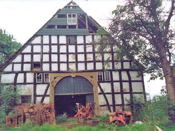 Backhaus Tengern Fachwerkgebäude mit großem Torbogen, umgeben von Bäumen und Ziegelstapeln an einem ruhigen Ort.