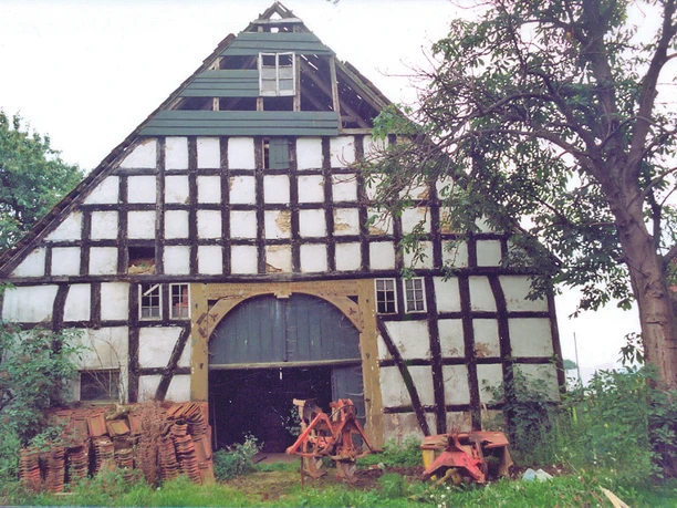 Backhaus Tengern Fachwerkgebäude mit großem Torbogen, umgeben von Bäumen und Ziegelstapeln an einem ruhigen Ort.