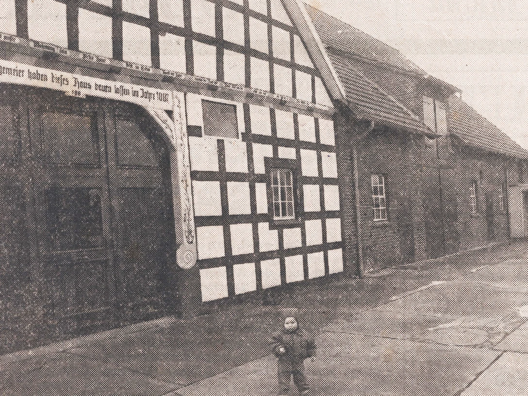 tengern-hof-jungemeier.jpg Historisches Fachwerkgebäude mit Torbogen, datiert 1815, altmodisch schwarz-weiß, kleines Kind vorne.