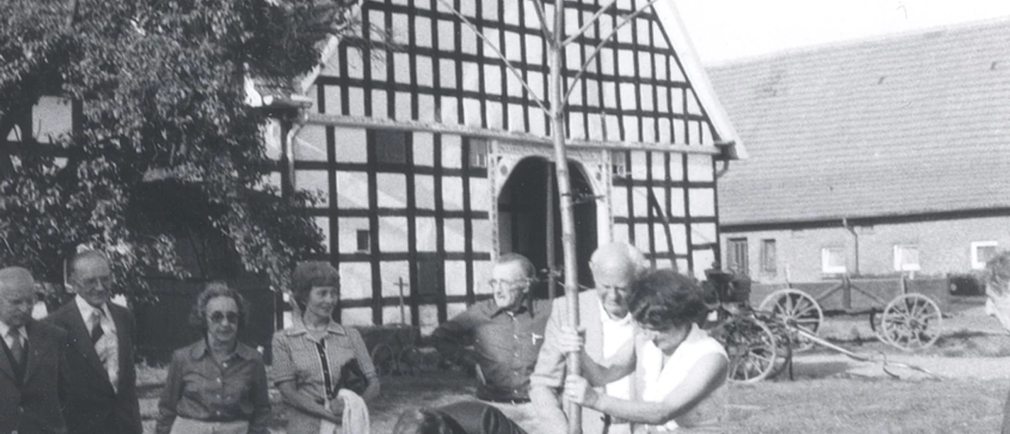 tengern-kahre-hof.jpg Eine Gruppe von Menschen pflanzt feierlich einen Baum vor einem historischen Fachwerkgebäude.