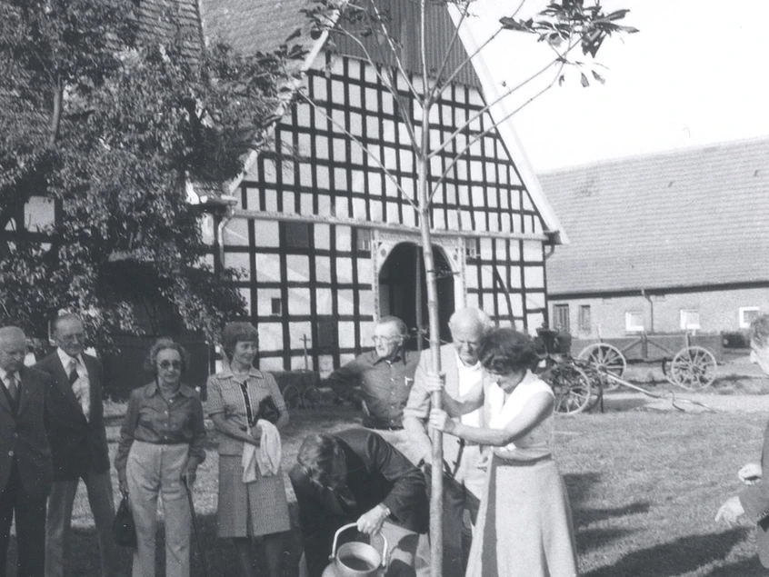tengern-kahre-hof.jpg Eine Gruppe von Menschen pflanzt feierlich einen Baum vor einem historischen Fachwerkgebäude.
