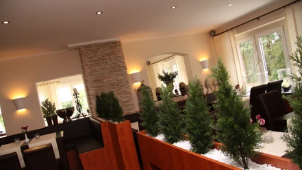 Restaurant im Landhaus Jägerkrug Helles Restaurant mit moderner Einrichtung, Steinwand, Pflanzen und großen Fenstern für Tageslicht.