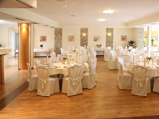 Saal im Landhaus Jägerkrug Eleganter Festsaal mit weiß gedeckten Tischen, Kerzenleuchtern und großen Fenstern mit Gartenblick.