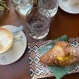 kaffeetisch.jpg Capuccino mit Schaum und Croissant auf Teller mit Puderzucker, auf Tisch mit Wasser und Gläsern.