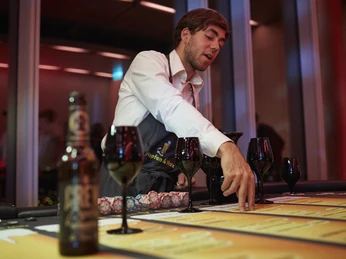 Hopfen & Malz. Bier-Poker Tisch. Dieter Jacobi.jpg Mann im weißen Hemd erklärt Karten an einem Tisch mit Weingläsern und Bierflasche.</p>Man in white shirt explaining cards at a table with wine glasses and beer bottle.</p> <p