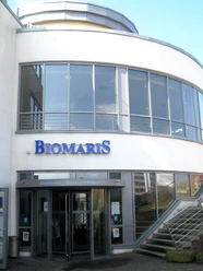 The BIOMARIS shop building in Borkum is located in the tidal land, with a modern glass and steel design, dominated by a large BIOMARIS logo.