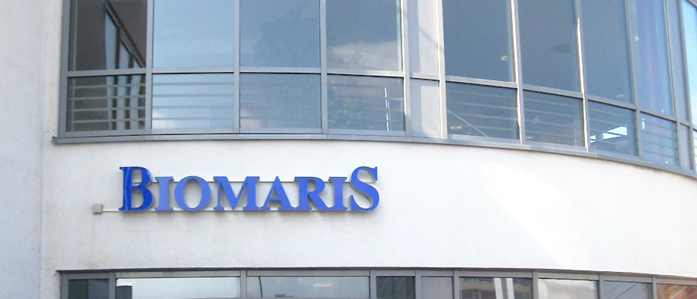2024-02_BIOMARIS_Shop_Borkum_Gezeitenland.jpg Das BIOMARIS Shop-Gebäude auf Borkum liegt im Gezeitenland, mit modernem Glas- und Stahl-Design, dominiert von einem großen BIOMARIS-Logo.