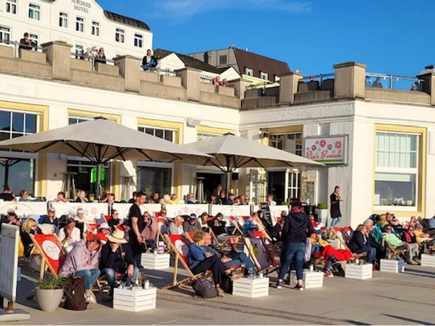 People relax on lounge chairs in front of a café on a sunny day in Borkum.