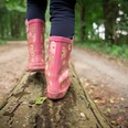 Waldwanderung Ein Kind balanciert in pinken Gummistiefeln auf einem Baumstamm im Wald.