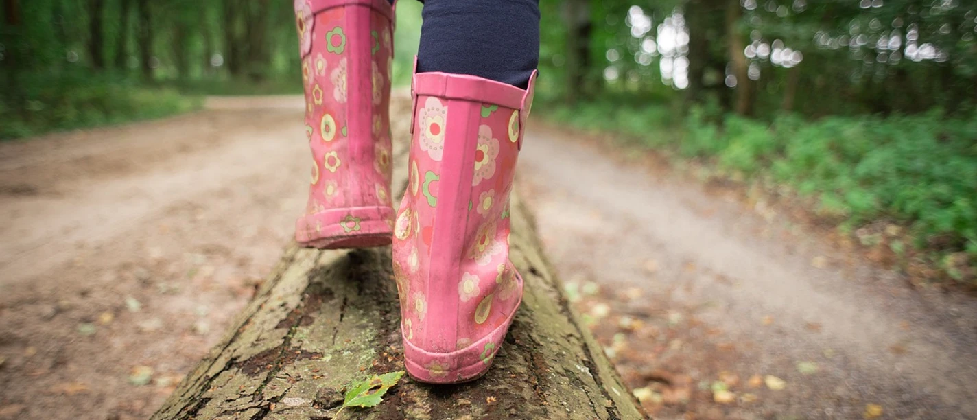 Waldwanderung Ein Kind balanciert in pinken Gummistiefeln auf einem Baumstamm im Wald.