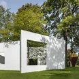 Skulpturenpark Weiße, rechteckige Skulptur im grünen Park, umgeben von hohen Bäumen, zeigt ein Fenster.White, rectangular sculpture in a green park, surrounded by tall trees, showing a window.