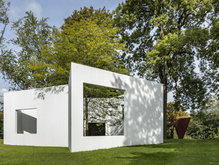 Skulpturenpark Weiße, rechteckige Skulptur im grünen Park, umgeben von hohen Bäumen, zeigt ein Fenster.White, rectangular sculpture in a green park, surrounded by tall trees, showing a window.