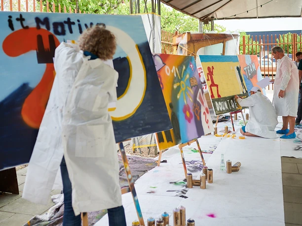 Cologne Graffiti. Teamarbeit People paint colorful graffiti on large canvases in a creative outdoor area.</p> <p