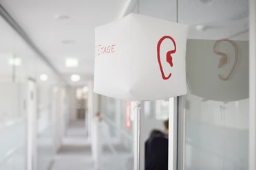 SINNfonie. Ein Parcours durch die Welt de Sinne Ein Flur mit moderner Beleuchtung und einem roten Ohrsymbol auf einer weißen Leuchte.