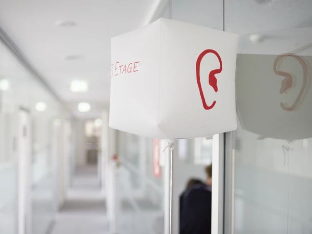 SINNfonie. Ein Parcours durch die Welt de Sinne A hallway with modern lighting and a red ear symbol on a white luminaire.