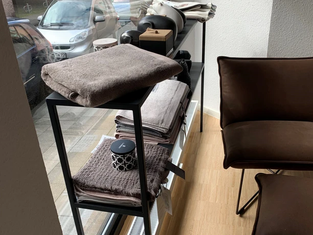Niedriges Regal vor einem Schaufenster mit Handtüchern und weiteren dekorativen Produkten.