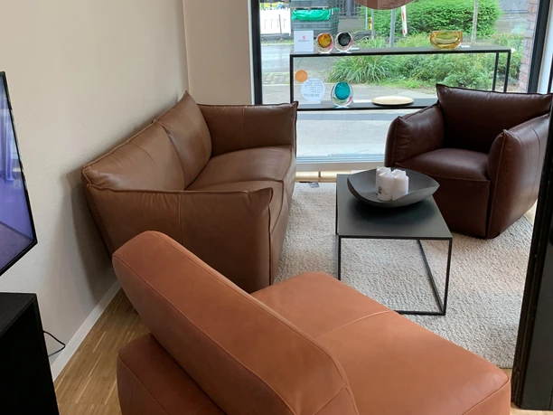 Ledercouch und zwei Sessel auf einem hellen Teppich mit einem runden Tisch in der Mitte.
