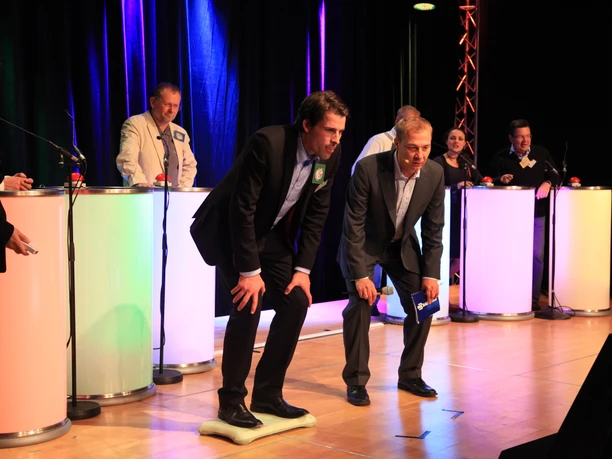 WeQuiz. Das Quizevent. Skispringen A quiz competition with two men in suits concentrating on buzzers on stage.