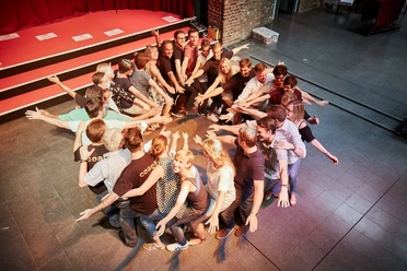 Westar. Zeigen was in uns steckt. Menschen bilden im Kreis stehend eine dynamische Pose mit ausgestreckten Armen auf einer Bühne.