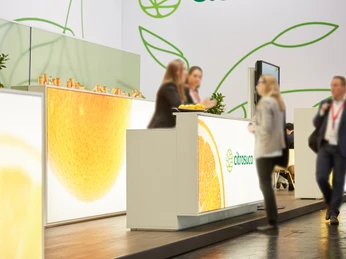 Citrosuco, Messeservice Die Messe zeigt Citrusco-Stand mit orangenen Motiven, Personen in Gesprächen, moderne Atmosphäre.The fair shows Citrusco stand with orange motifs, people in conversation, modern atmosphere.