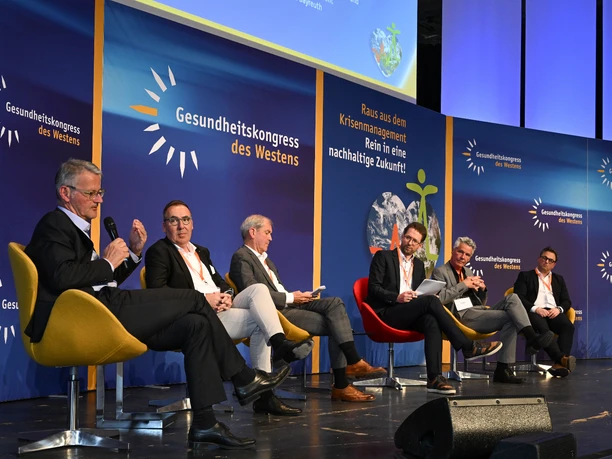 Gesundheitskongress des Westens 2023 Gesundheitskongress: Sechs Personen diskutieren auf einer Bühne mit blauen Bannern im Hintergrund.