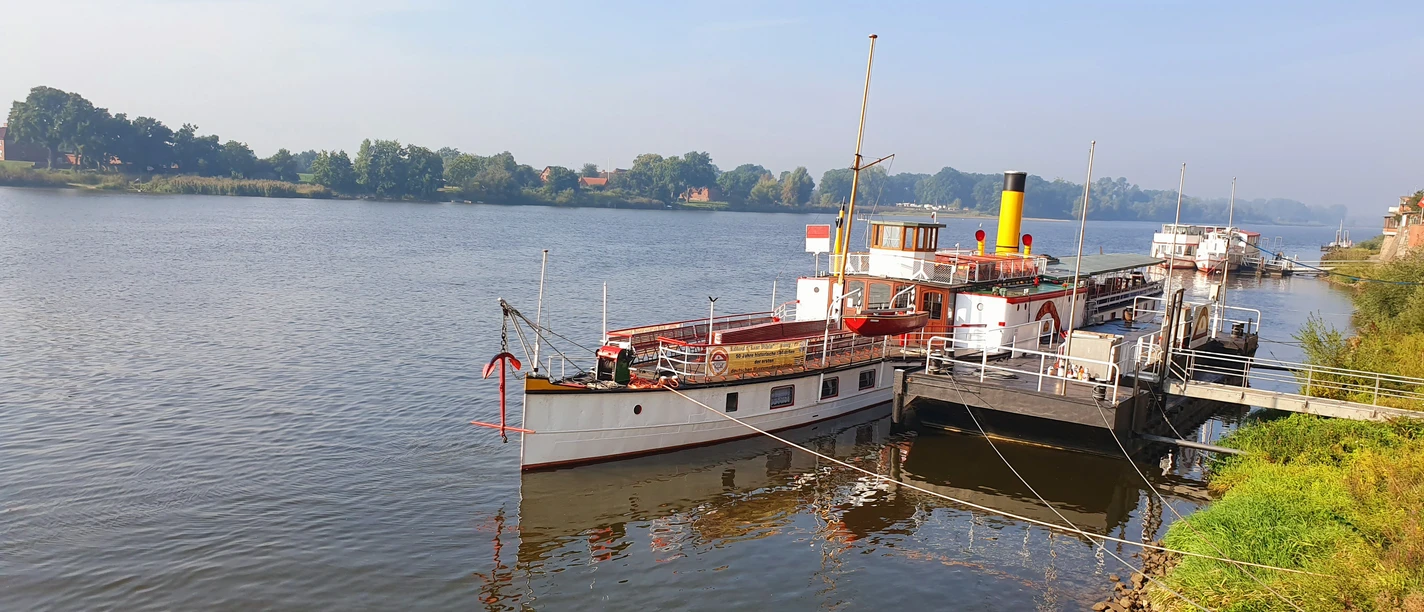 KaiserWilhelm©Dorothee Meyer (11).jpg Historic paddle steamer moored at a riverside pier on a calm, wide river under clear sky