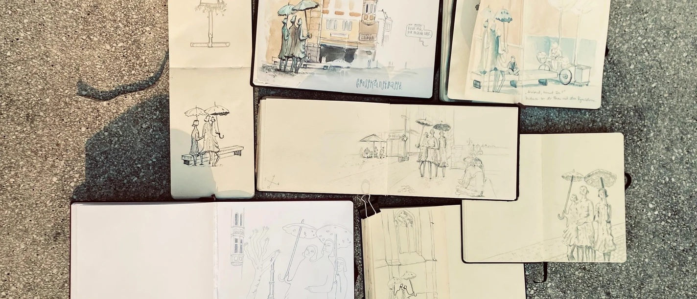 Urban Sketchers Mehrere geöffnete Skizzenbücher auf dem Boden zeigen unterschiedlich detaillierte urbane Zeichnungen von Straßenszenen mit Menschen und Architektur.