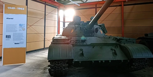 05_DPM_Neue Dauerausstellung_Bereich Kalter Krieg I-min.jpg Ein grüner Panzer aus der Zeit des Kalten Krieges steht in einem Ausstellungsraum neben einer Informationstafel.