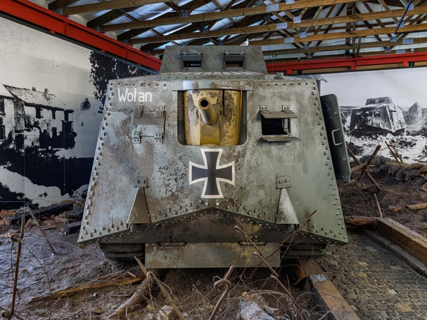 06_DPM_A7V front mitte-min.jpg Das Bild zeigt die Frontansicht eines historischen deutschen Panzers, des A7V, aus dem Ersten Weltkrieg. Der Panzer, mit der Bezeichnung "Wotan", präsentiert sich in einem Museum auf einer nachgestellten Schlachtfeld-Szenerie.