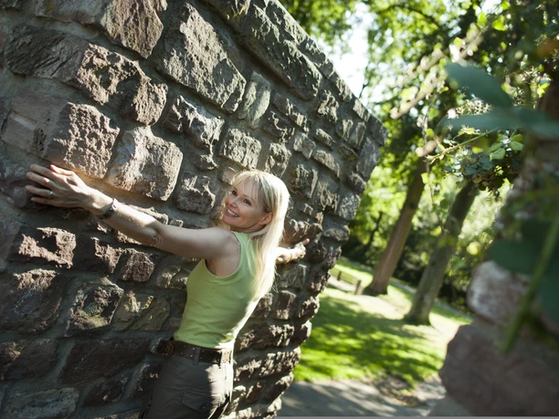 Frau mit ausgebreiteten Armen an der Stadtmauer