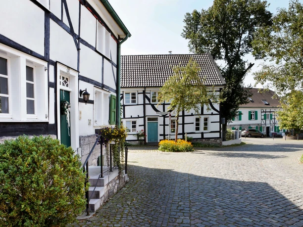 Haan-Gruiten nach Wülfrath-Düssel - Karl-Heinz Hadder Fachwerkhäuser mit weißen Wänden und dunklen Balken stehen an einer kopfsteingepflasterten Straße.