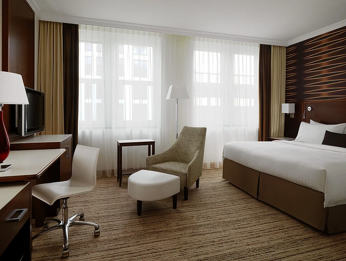 Deluxe King Zimmer <p>Modernes Hotelzimmer mit Doppelbett, Schreibtisch, Stuhl, Sessel und großem Fenster.</p>