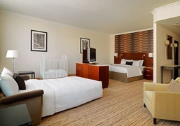 Familienzimmer 2 Helles Hotelzimmer mit zwei Betten, Babybett, Sessel, Lampe, Fernseher und moderner Wandgestaltung.</p>Bright hotel room with two beds, baby crib, armchair, lamp, TV and modern wall design.</p> <p