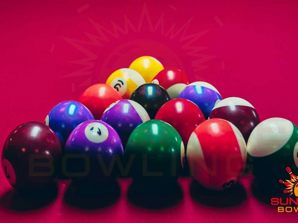 Sunshine Bowling Pirna Bunte Bowlingkugeln sind auf einem roten Tisch angeordnet, im Hintergrund das Logo von Sunshine Bowling.