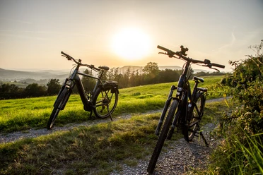 Radfahrer Lügde Zwei Fahrräder stehen auf einem Feldweg bei Sonnenuntergang, umgeben von grünen Wiesen.