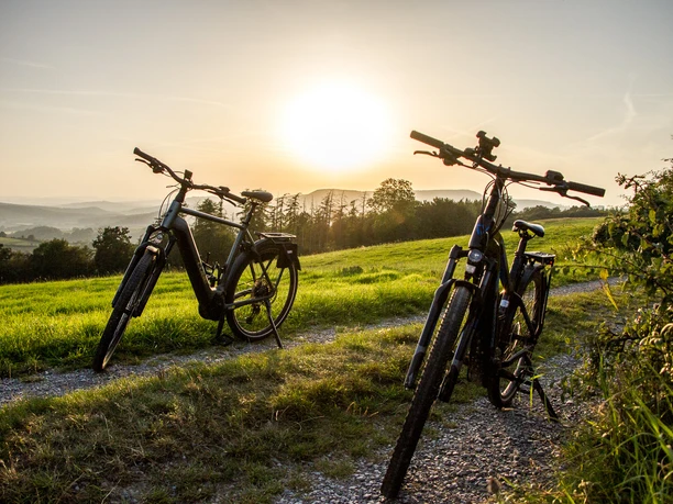Radfahrer Lügde Zwei Fahrräder stehen auf einem Feldweg bei Sonnenuntergang, umgeben von grünen Wiesen.