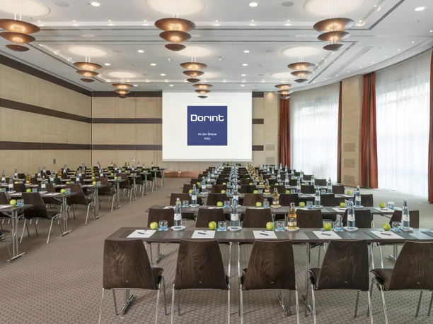 Berlin A+B Tagungsraum mit grauem Teppich, Tischen, Stühlen und Leinwand für Präsentationen.</p>