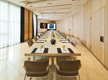 Brüssel A+B Ein moderner Konferenzraum mit langer Tafel, Stühlen, Schreibunterlagen und Präsentationsbildschirm.A modern conference room with a long table, chairs, writing pads and a presentation screen.