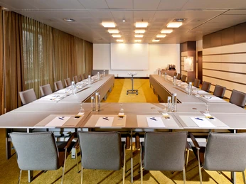 Martin + Augustin Ein moderner Konferenzraum mit U-förmig aufgestellten Tischen und lederbezogenen Stühlen.A modern conference room with U-shaped tables and leather-covered chairs.